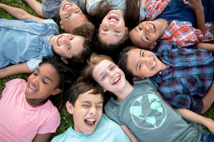 Photo of children laying down  with their heads together in a circle