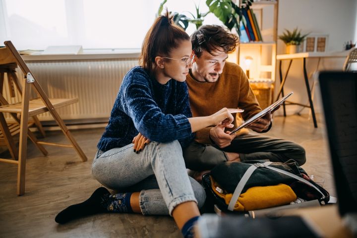 Photo of a man and women looking at a tablet together sitting on the floor in their home